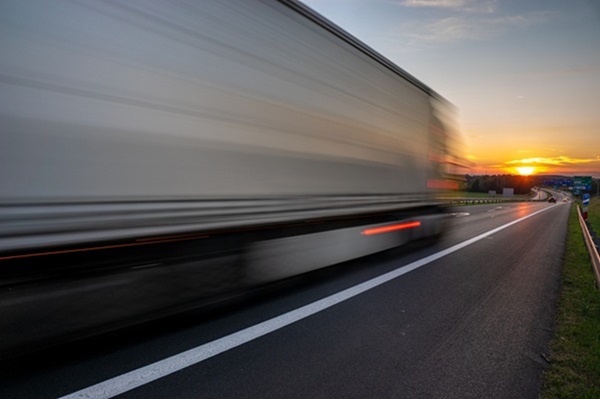 Blurred view of a large commercial truck driving on a highway at sunset, with motion lines indicating high speed. (384940312)
