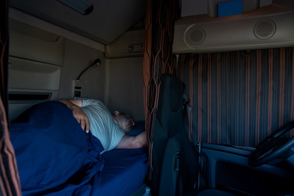 Truck driver sleeping in the cab of his truck at night with cabin curtains drawn. (595531151)